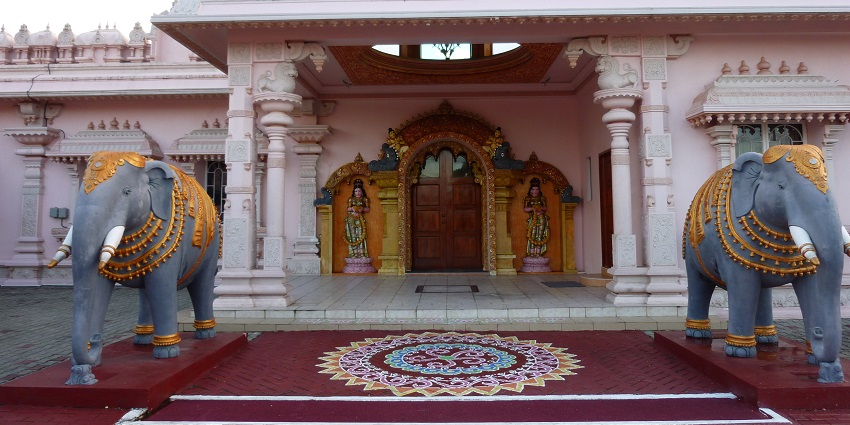 A picture of the entrance of a temple having two elephant statues placed adjacent to the doors