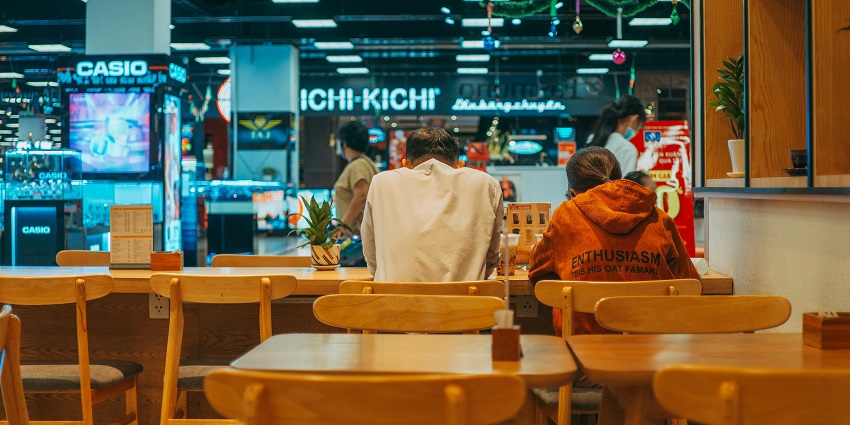 An image of people sitting at the wooden tables waiting for food in a food court.