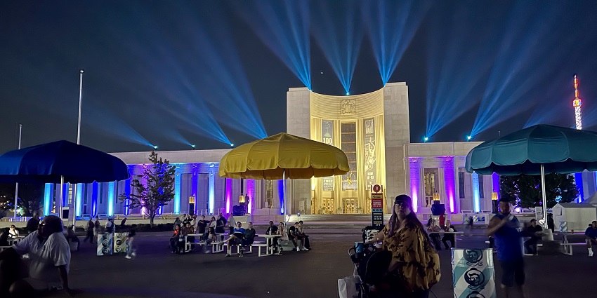 Fair Park of Dallas at night lit up with colourful lights, people sitting and eating.