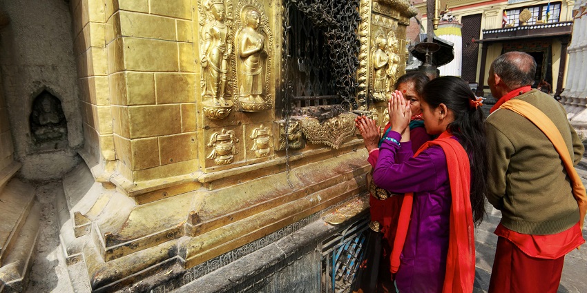 An image of people praying while with folded hands and ritual garlands around their necks.