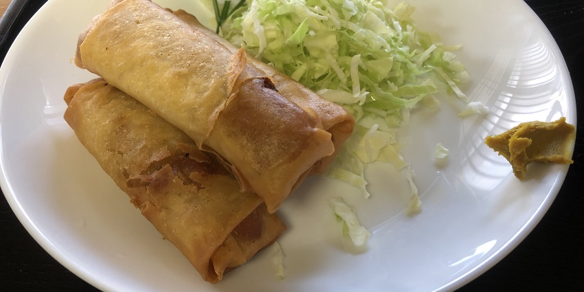 A spring roll platter consisting of two spring roll pieces is served with chopped cabbage