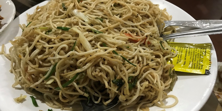 piping hot noodles being served on the ceramic plate and with the salad over it.