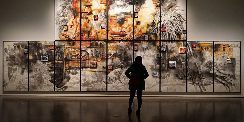 A picture of a woman standing in an art gallery and admiring the art pieces placed on the wall in front of her