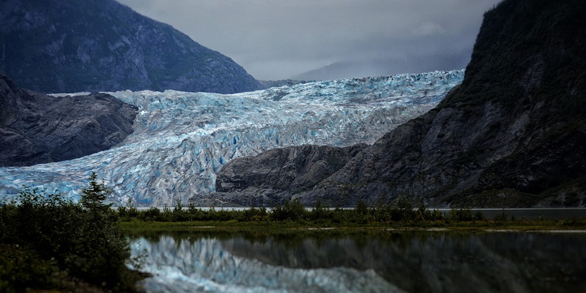 A glacier amidst two mountains near a lake with its reflection in it
