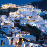 Santorini island at night with well-lit buildings and people enjoying the restaurant