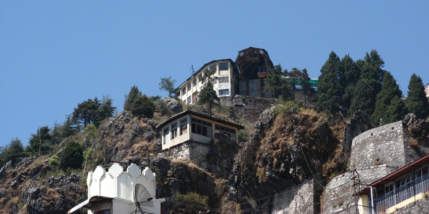 A picture of a scenic hill station with a house on top, located in Uttarakhand
