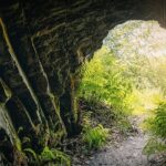 A large cave opening of the Gupta Dham caves, gazing out towards a scenic view of lush greenery