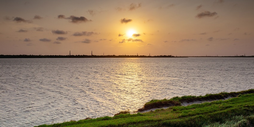 A picture of a beach with the sun setting behind the sea, creating a golden hour