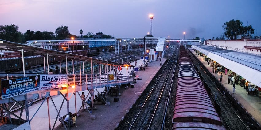 A view of a busy train station in India with travellers walking along the platform.