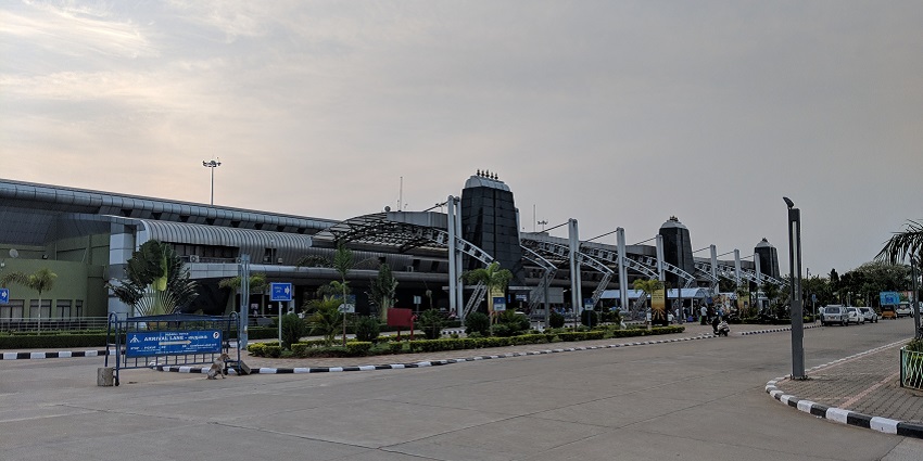 Trichy Airport terminal with modern architecture, glass windows, and parked vehicles.