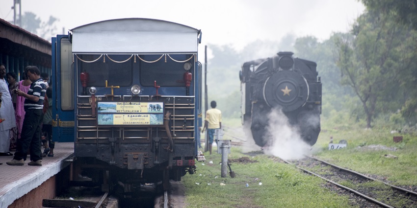 Mettupalayam railway station with trains leaving tracks and people waiting at the platform.