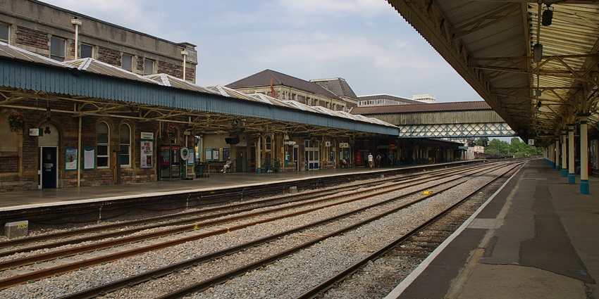 A railway station showing a railway track with enquiry windows in the corridor and people waiting.
