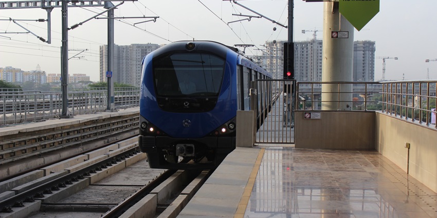 A blue and black metro arriving at the Koyambedu metro station with an empty platform