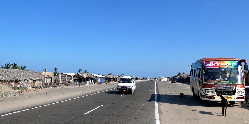 Dhanushkodi bus stop with huts on one side of the road and a bus parked on the other.