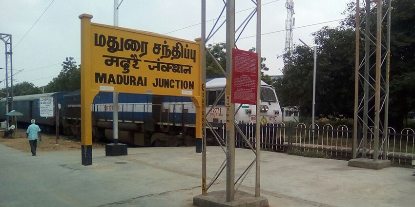 Madurai railway station with a train, a signboard and a person walking on the platform.