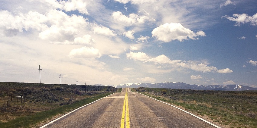 Empty countryside road stretching into the horizon, surrounded by green fields under a cloudy sky
