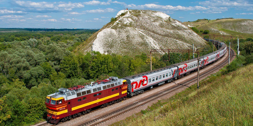Train winding through scenic hills, surrounded by lush greenery and majestic landscapes under a clear sky