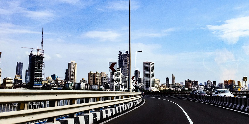A bustling Mumbai road with heavy traffic, lined with tall buildings and city landmarks