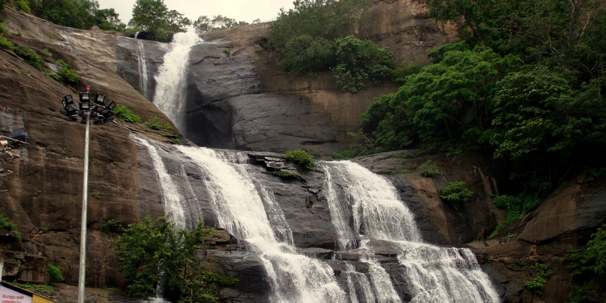 An image showing the flowing Courtallam Waterfalls cascading over uneven rocky surfaces.