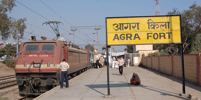 An Indian street view with a locomotive pulling a passenger train near Agra Fort railway station.