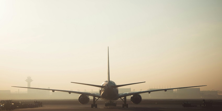 An aeroplane flying high in a clear blue sky, with clouds scattered in the background.