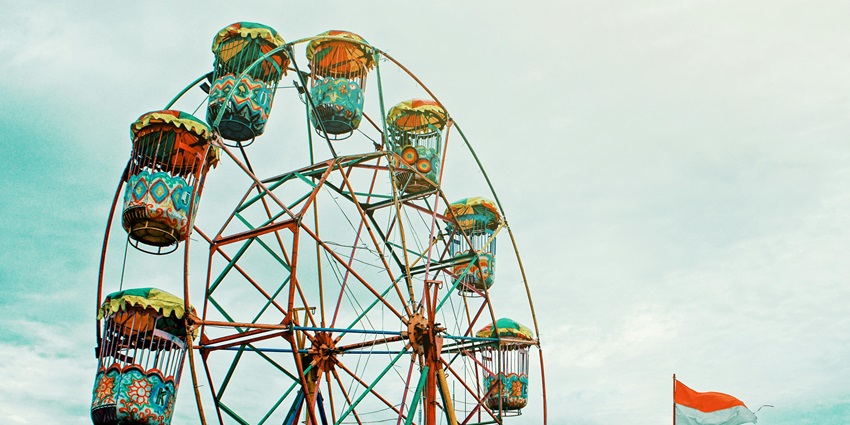 Image showing an orange Ferris wheel beside a white and orange flag against a clear sky.