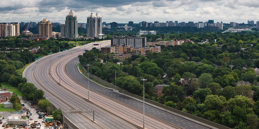 Evacuated highway road showing skyscrapers in front and lush greenery on one side of the highway