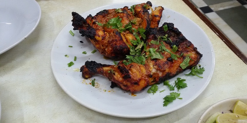 Well-cooked pieces of tandoori chicken are placed on a platter garnished with coriander