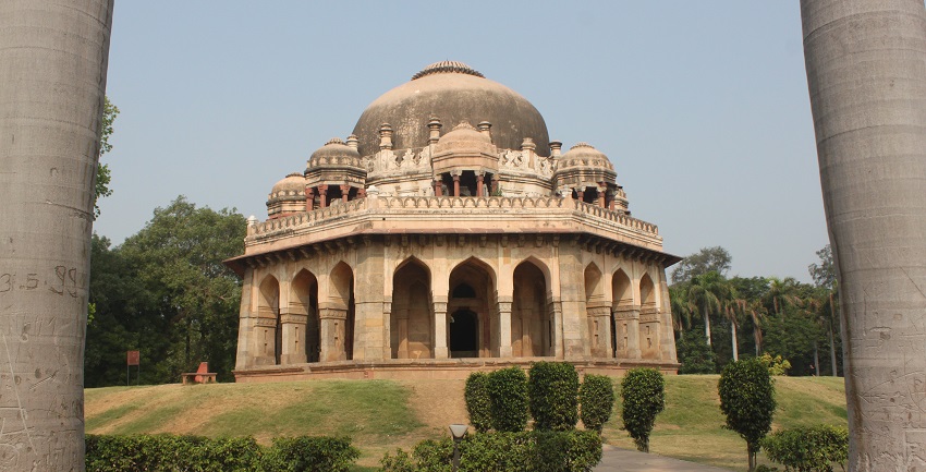A picture of a historical building with Mughal architecture, surrounded by lush greenery, taken from a distance