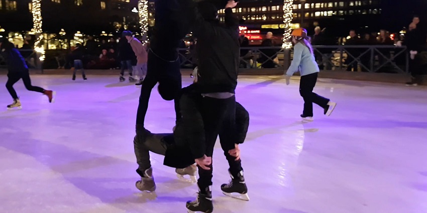 People enjoy ice skating together on a smooth indoor rink under beautiful Christmas lights.