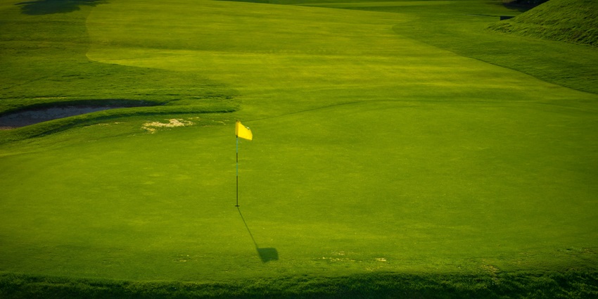 A bright yellow flag marks the hole on a neatly manicured green at a sunlit golf course.
