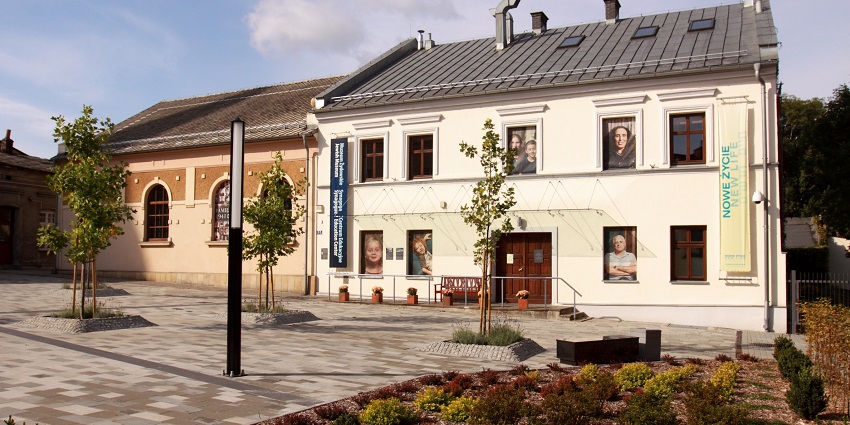 Jewish centre and museum complex with sign flags, posters on windows and small plants.
