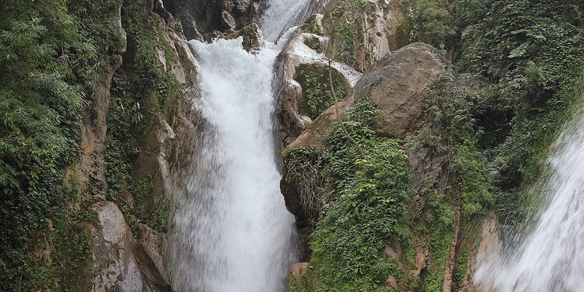 A picture of a majestic waterfall cascading down a lush green mountain in Uttarakhand