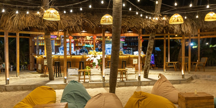 Jojo beach bar with decorations, sofas, tables, chairs, carpets and a wooden roof