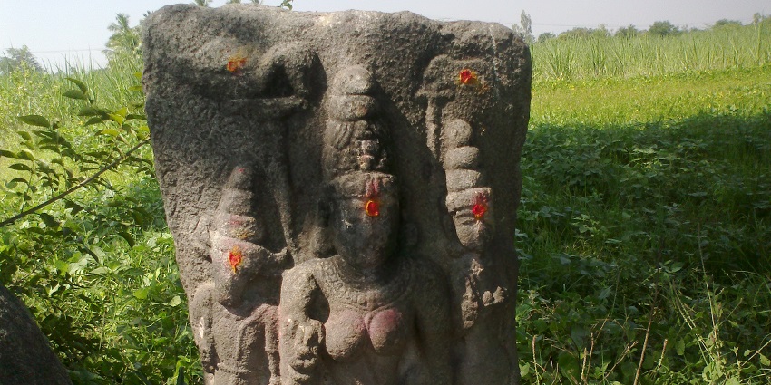 Jambai Malai Jyestha Devi statue, surrounded by greenery under a clear blue sky.