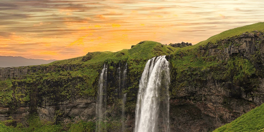 Kaalikesam Waterfalls cascading down mountains into a river, surrounded by lush greenery.