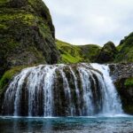 A stunning waterfall flows down rocky cliffs surrounded by greenery and trees.