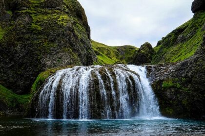 A stunning waterfall flows down rocky cliffs surrounded by greenery and trees.