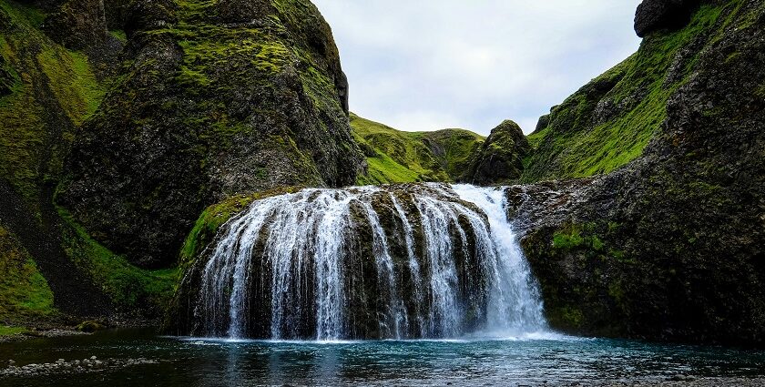 A stunning waterfall flows down rocky cliffs surrounded by greenery and trees.