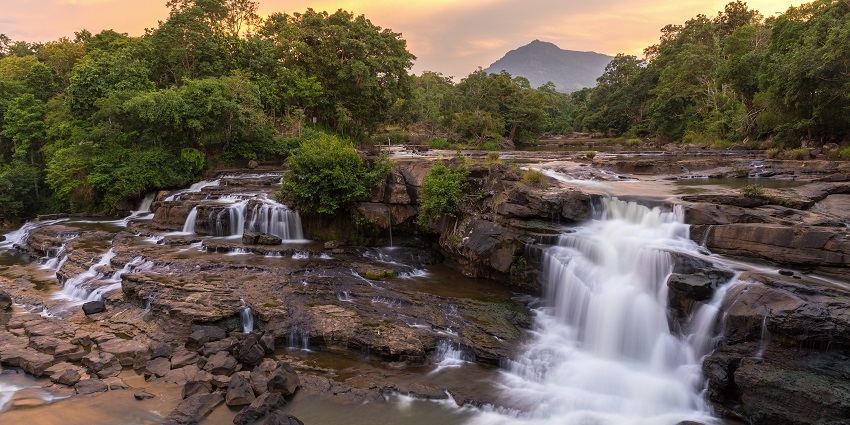 An image of Kalhatti waterfall cascades down rocky cliffs, creating a refreshing mist that fills the air