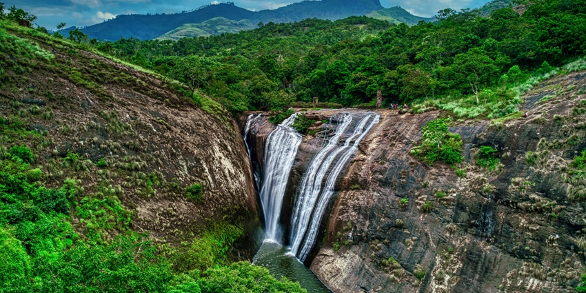 Cascading waters of Kallatty Falls flowing through rocky terrain amidst dense green forest.