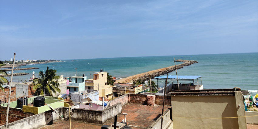 A view of Kanyakumari Beach, showcasing golden sand, gentle waves, and top hills.