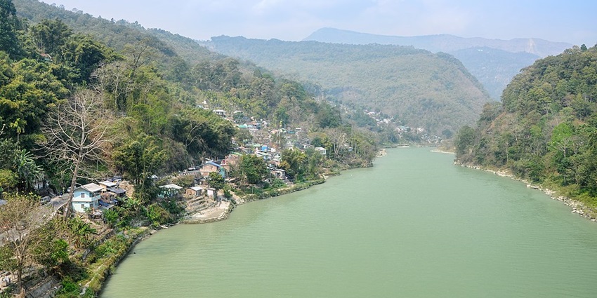 A serene view of the River flowing, surrounded by lush greenery and distant hills under a clear blue sky.
