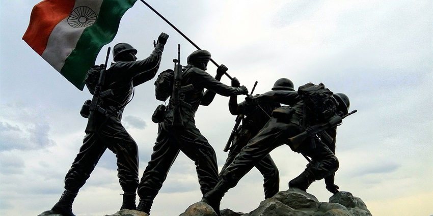 A tall statue of an Indian soldier saluting, with the Indian flag waving beside him.