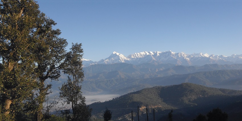 A panoramic view of green hills and valleys under a clear blue sky in Kausani, India.