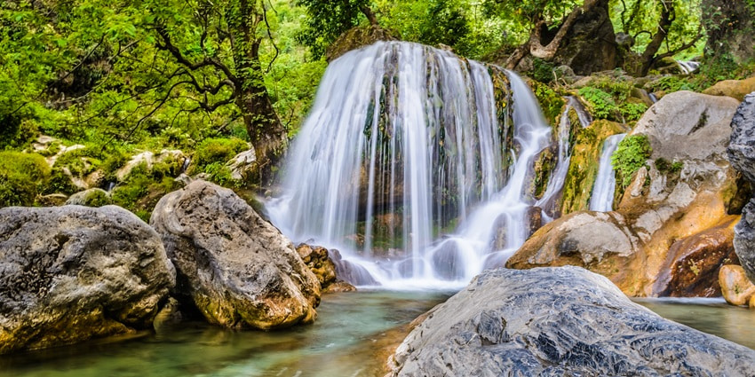 A picture of a majestic waterfall with a stream of water cascading down a lush green hill