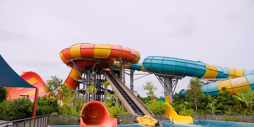 An image showing a colourful water slide spiralling down into a bright blue swimming pool