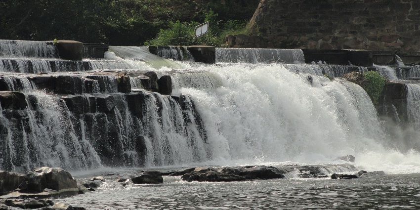 Kodiveri Falls cascading down rocky formations into the water surrounded by lush greenery.