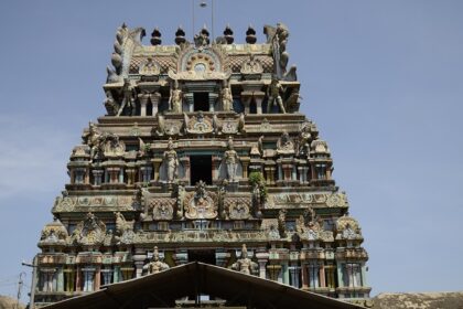 Kolanjiappar Temple featuring entrance and a woman worshipping and small shops nearby