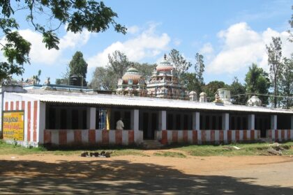 Kollimalai temple with striped walls, domed towers, and surrounding trees under a blue sky.